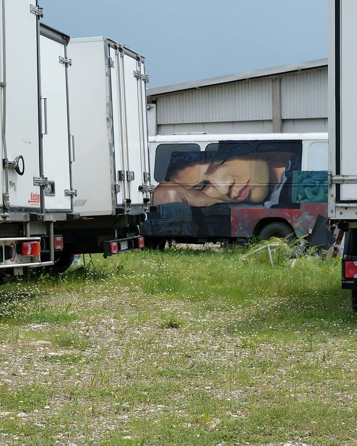 Colorful murals by Artez featuring a large portrait on a vehicle parked among white trucks in an open grassy area.