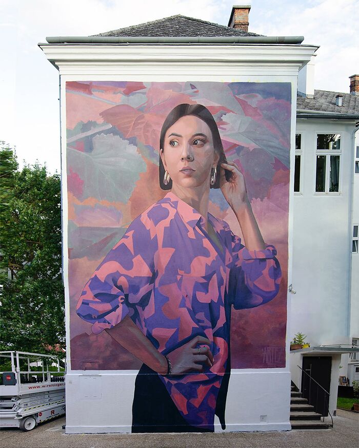 Large colorful mural by Artez depicting a woman in a patterned shirt painted on a city building wall.