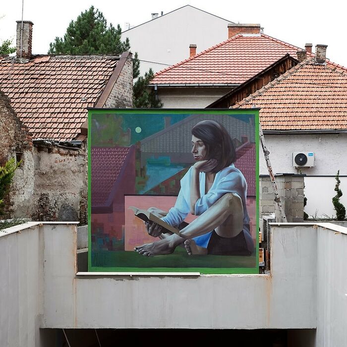 Colorful mural by Artez depicting a woman reading, enhancing urban space with vibrant city art.