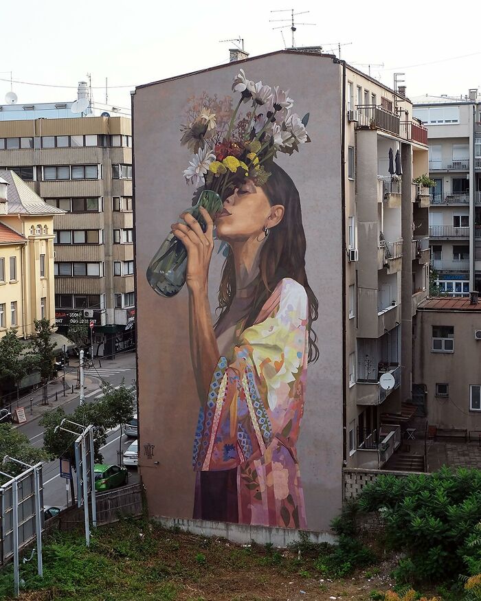 Colorful mural by Artez of a woman holding flowers on a city building wall, blending urban life with vibrant street art.