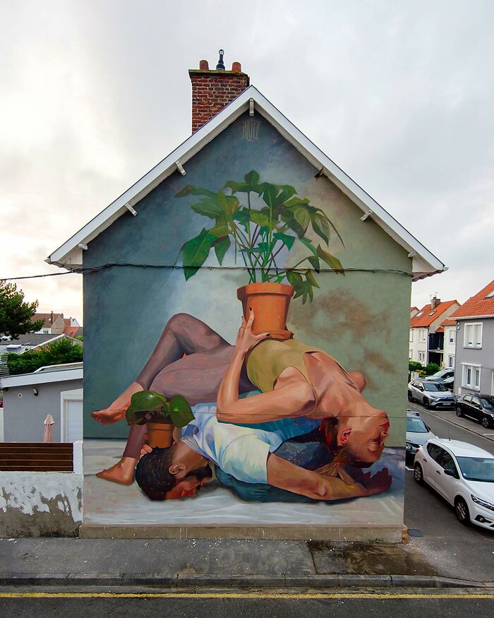 Colorful mural by Artez on a house wall showing two intertwined figures holding potted plants, brightening urban surroundings.
