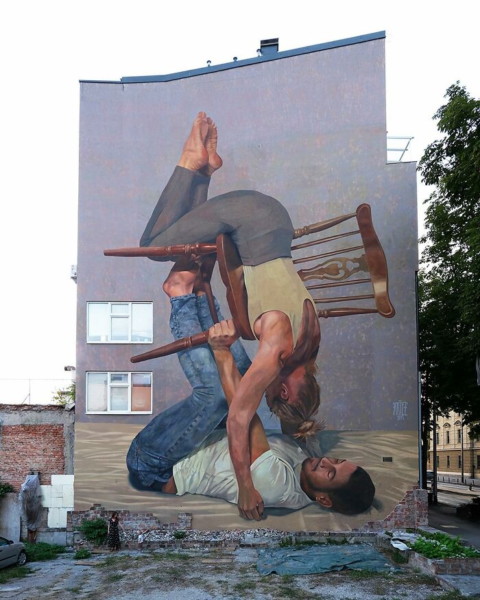 Large colorful mural by Artez depicting a man and woman balancing on a chair, enhancing urban city life vibrancy.