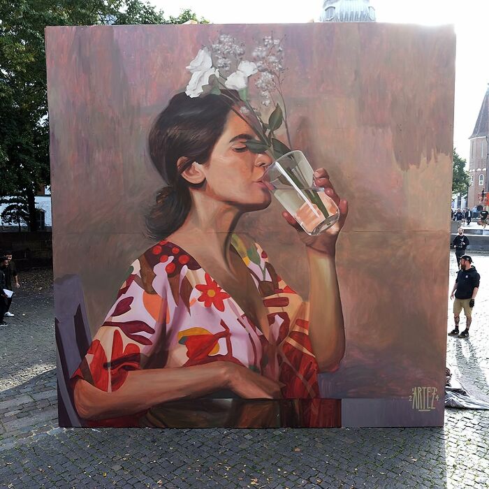 Large colorful mural by Artez depicting a woman drinking water with flowers, brought to life in an urban city setting.