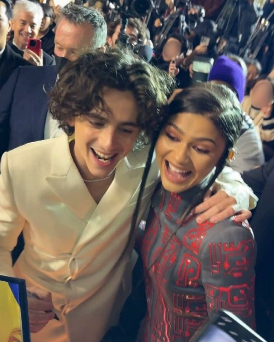 Timothée Chalamet smiling and posing with a Zendaya at a crowded event, surrounded by fans and photographers. Timothée Chalamet smiling and posing with a Zendaya at a crowded event, surrounded by fans and photographers.