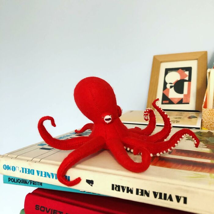 Red felted octopus sculpture with detailed tentacles displayed on a stack of books as felted artwork.