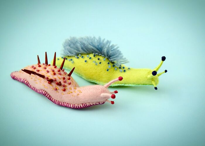 Two colorful felted artworks resembling spiky and fuzzy sea slugs on a light blue background, showcasing cute felted art.