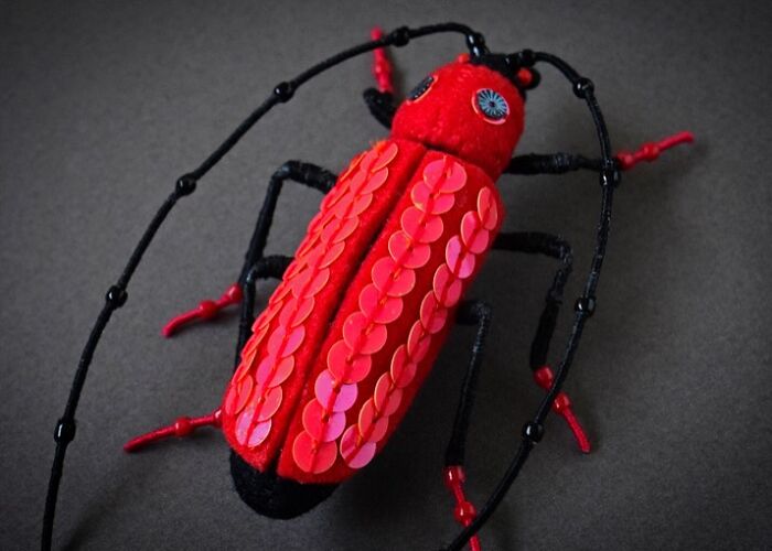 Red and black felted insect artwork with detailed sequins and wire legs, showcasing unique felted artworks craftsmanship.