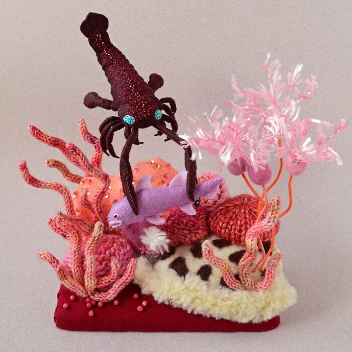 Felted artwork of a lobster holding a fish surrounded by pink coral and sea plants in a colorful underwater scene.