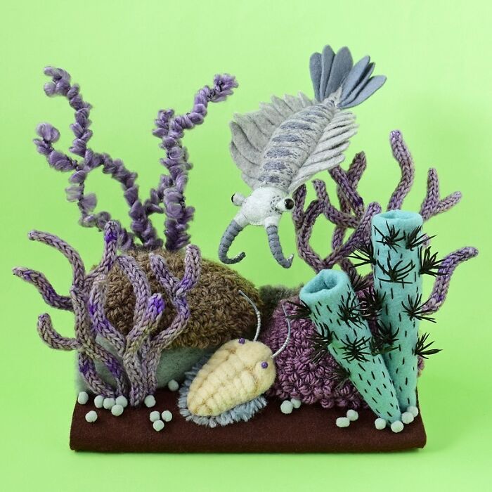 Felted artworks of sea creatures and coral in purple, blue, and beige colors against a green background.