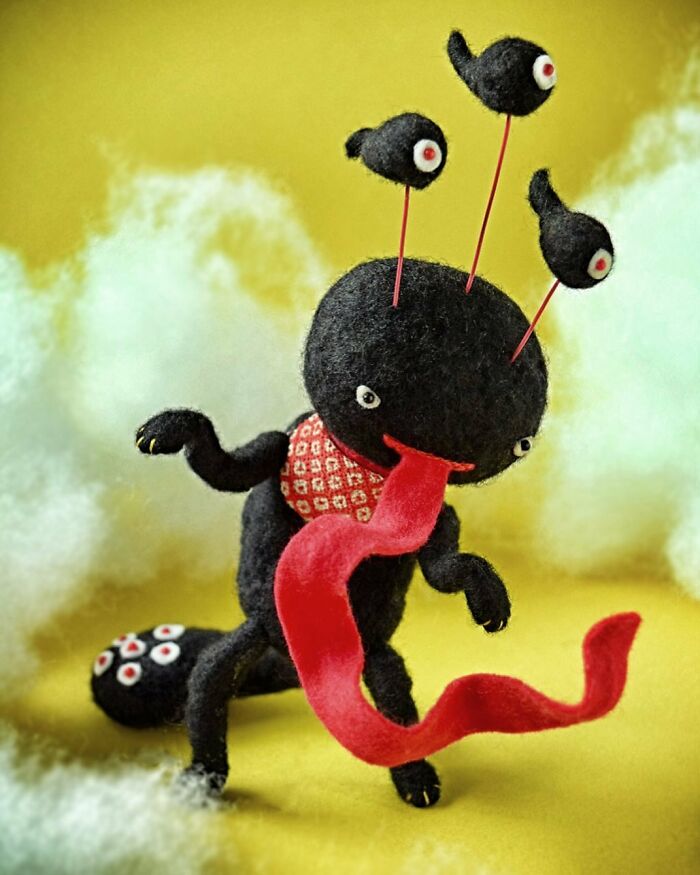 Black felted creature with multiple red-eyed antennae and a long red tongue, showcasing unique felted artworks.