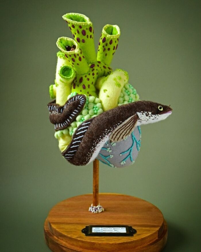 Felted artwork of a green coral reef and brown eel sculpture displayed on a wooden stand, showcasing unique felted art.