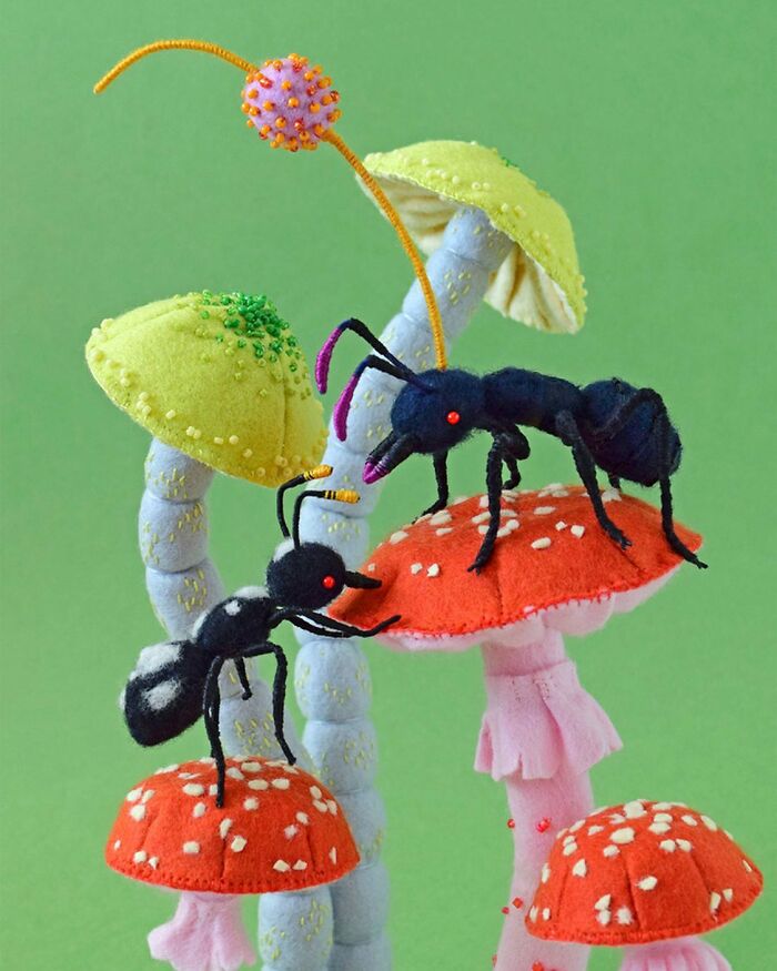 Felted artworks of colorful ants on whimsical mushrooms with detailed stitching and vibrant colors on green background.