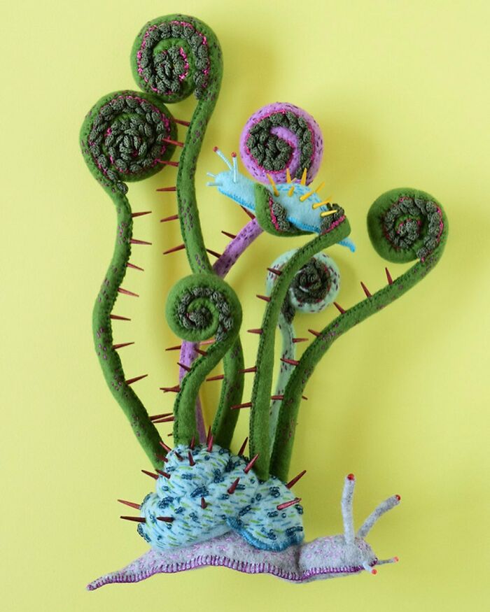 Felted artwork of a whimsical snail and curled plants with textured details and colorful stitched accents on a yellow background