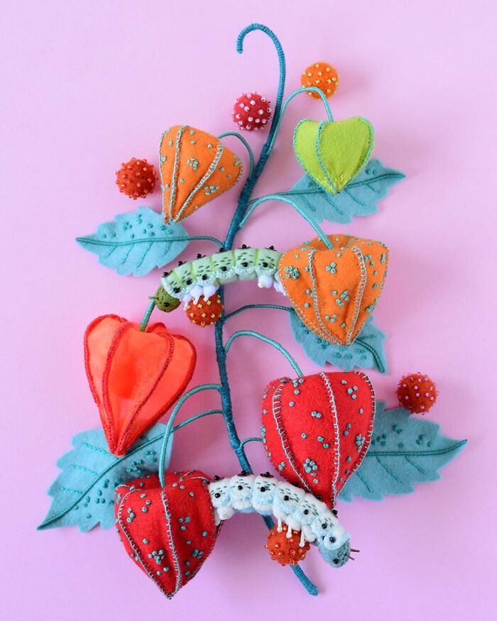 Colorful felted artworks featuring detailed leaves, flowers, and caterpillars on a pink background.