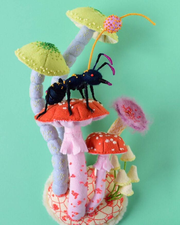 Felted artworks featuring colorful mushrooms and a black ant with intricate bead details on a teal background.