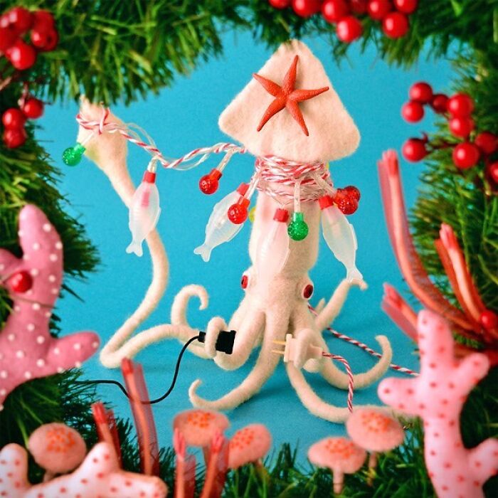 Felted squid artwork decorated with holiday lights, surrounded by felted coral and berries on a blue background.