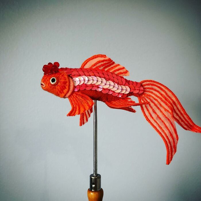 Red felted fish artwork with sequins and detailed fins displayed on a stand, showcasing unique felted artworks.