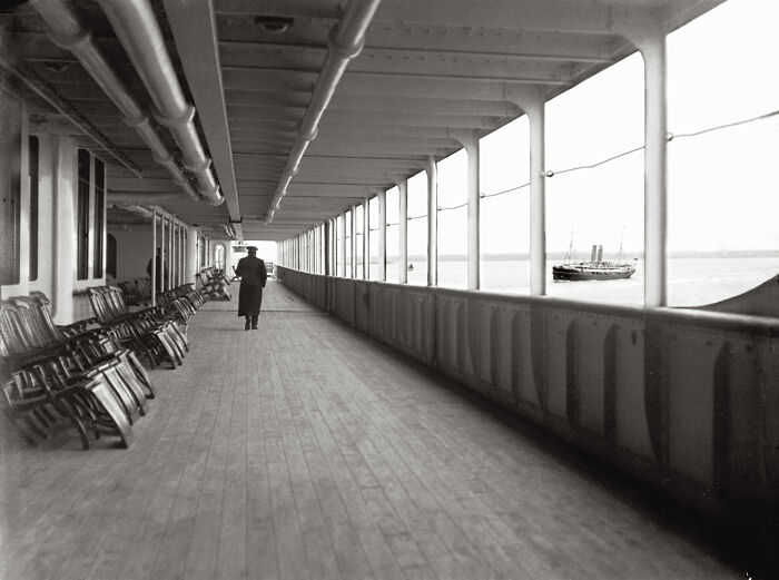 Rare historical photo of the Titanic deck showing a lone figure walking along wooden floors with chairs lined against the railing.