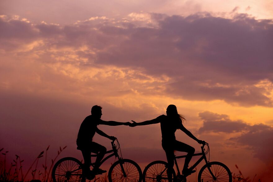 Silhouettes of a couple on bicycles holding hands at sunset, symbolizing red flags in a relationship.