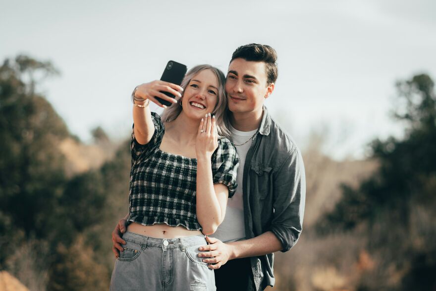 Young couple taking a selfie outdoors, smiling and embracing, illustrating red flags in a relationship masquerading as green lights.