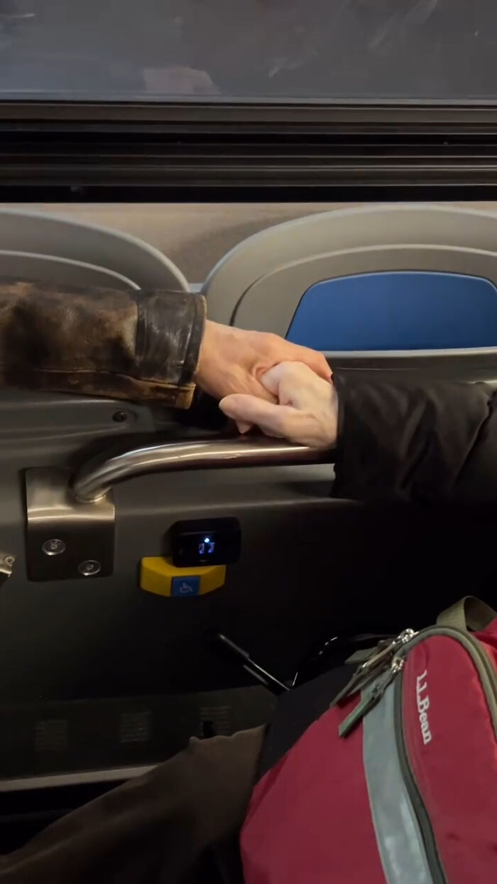 Two people holding hands on a New York subway surrounded by bags and seating, showcasing unique items carried by riders.