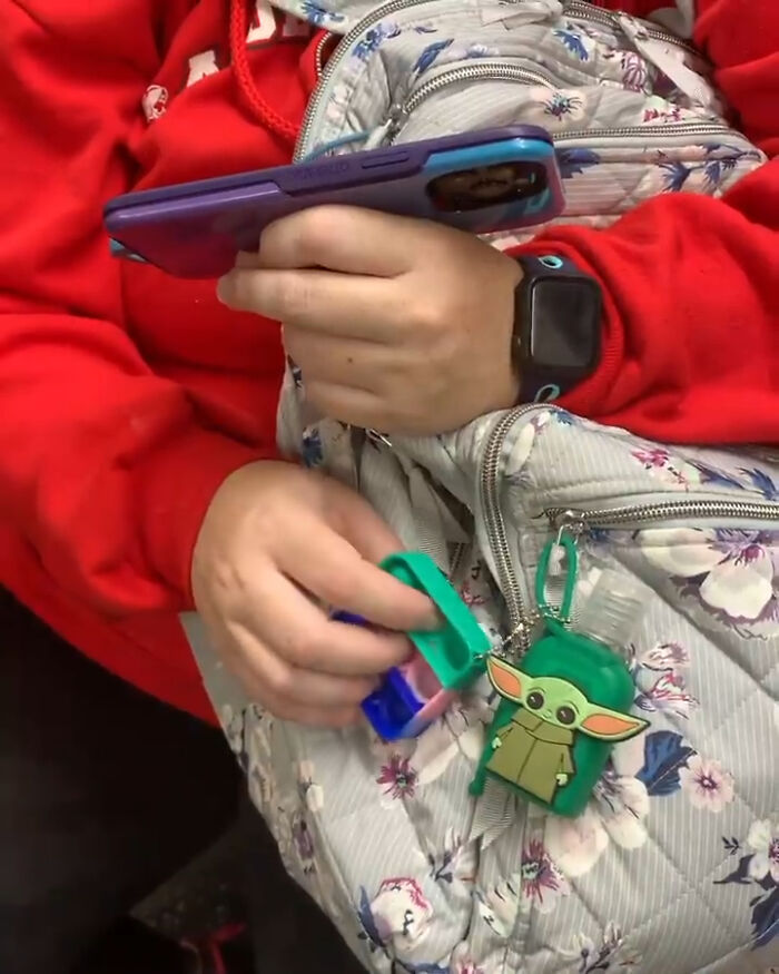 Person on New York subway holding colorful gadgets and a floral bag with a cute Grogu keychain attached.