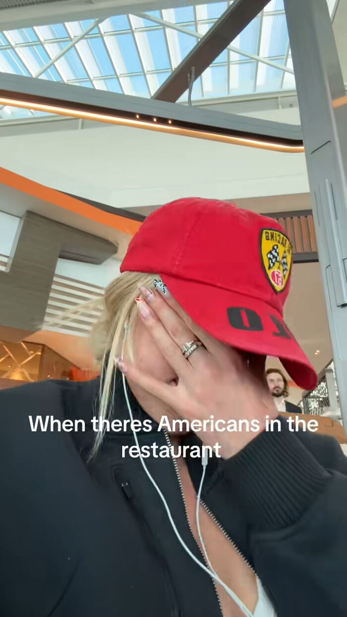 Olympic gold medalist Keely Hodgkinson covering her face wearing a red cap inside a modern restaurant setting.