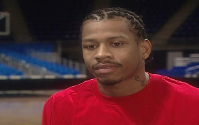 Man with braided hair in red shirt sitting indoors, reflecting on meeting an idol that changed his entire life.