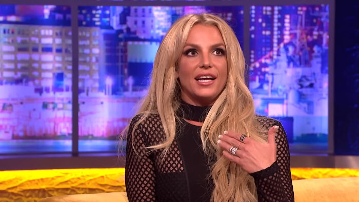 Blonde woman sharing a story about meeting an idol on a brightly lit TV show set in a casual interview setting.