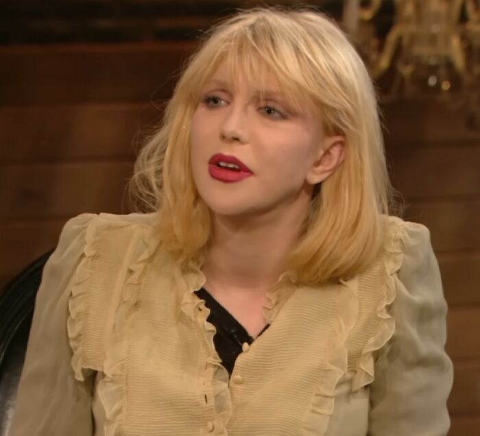 Blonde woman in beige ruffled blouse speaking during an interview about meeting an idol experiences.