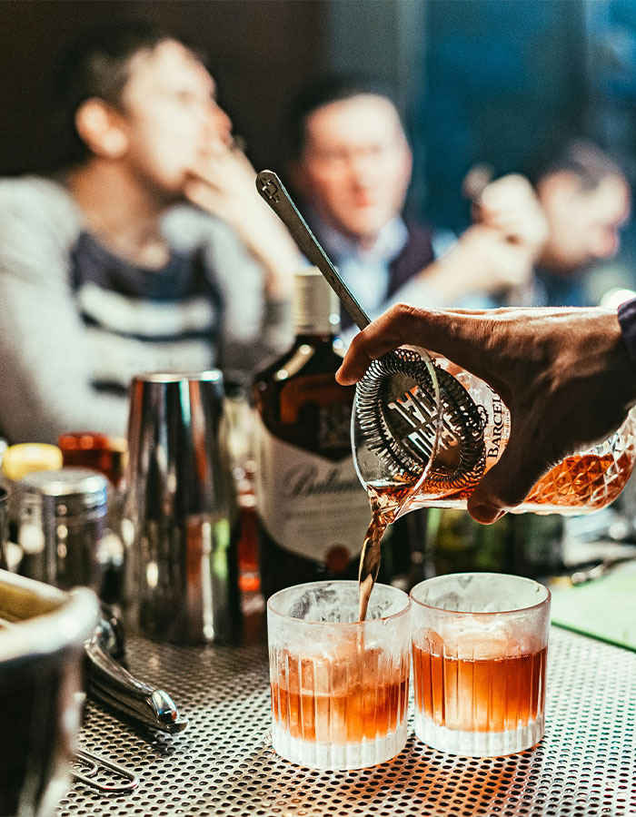 Bartender pouring cocktails at a pub bar with people socializing, highlighting woman told to cover up double standards.