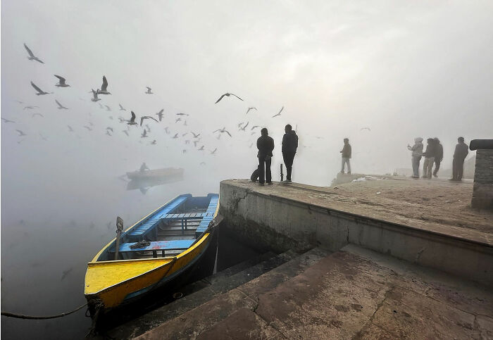 Foggy morning in Istanbul with people standing by the dock near a yellow boat and birds flying overhead.