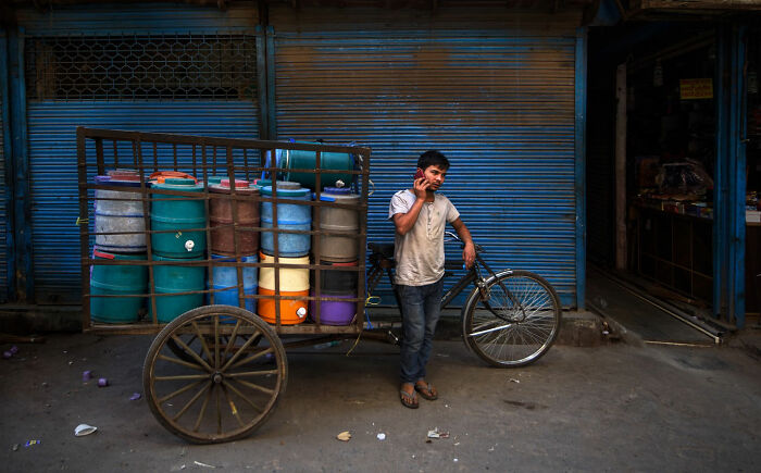 Young man talking on phone while standing beside a cart with colorful barrels in everyday life in Istanbul street scene