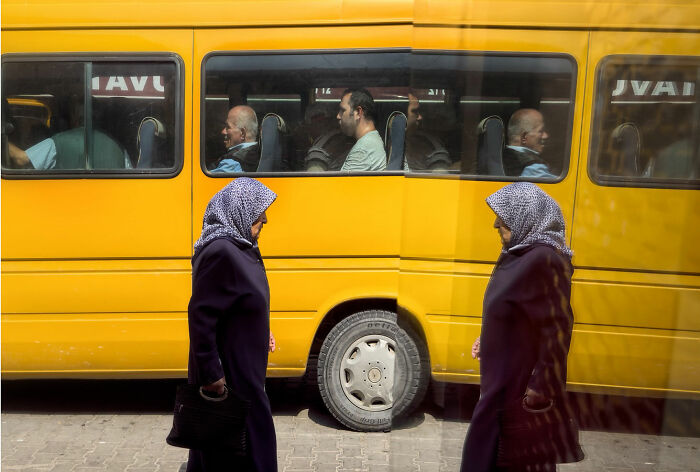 Woman walking past yellow bus with passengers inside, capturing candid moments of everyday life in Istanbul.