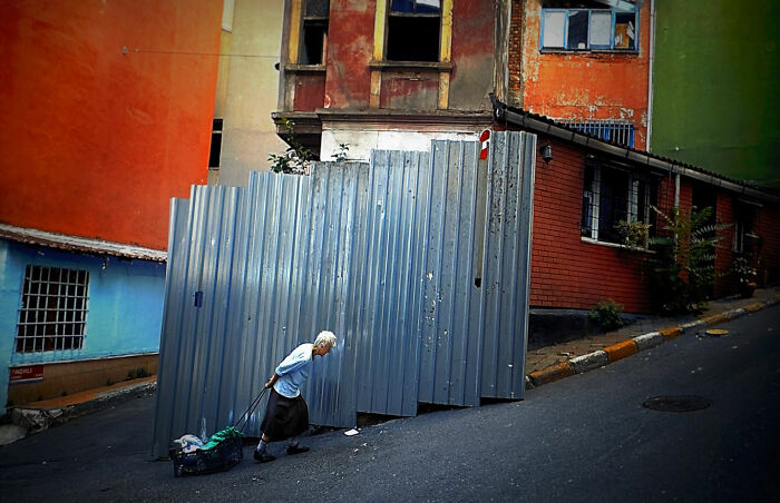 Elderly woman pulling a cart uphill along urban street, capturing candid moments of everyday life in Istanbul.
