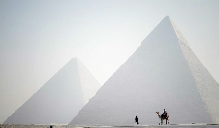 Pyramids in mist with a person walking and another riding a camel, an everyday life scene in Istanbul.