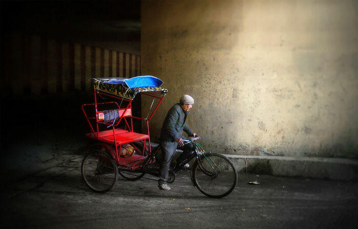 Man pushing a traditional red rickshaw in a dimly lit urban setting, capturing candid moments of everyday life in Istanbul.