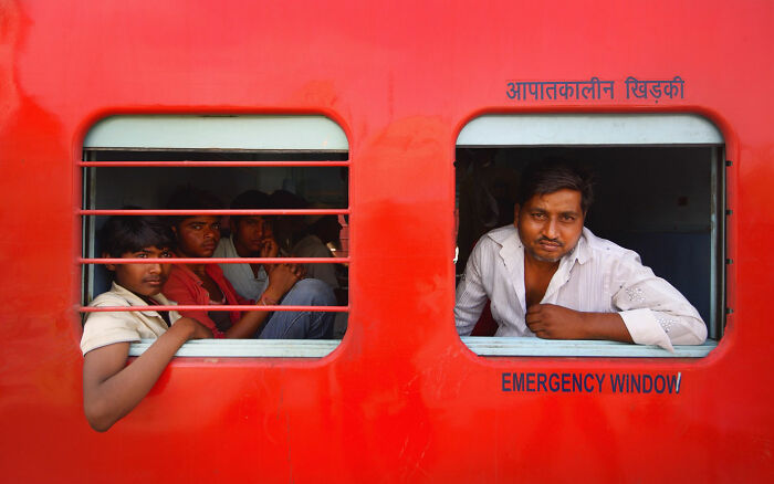 Group of men sitting and leaning out of a bright red train window, capturing candid moments of everyday life in Istanbul.