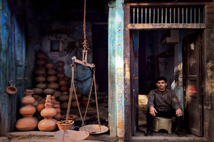 Man sitting in doorway of a pottery shop with clay pots and traditional scales, capturing everyday life in Istanbul.