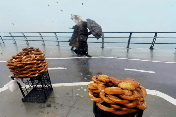 Street vendors selling simit in Istanbul on a rainy day with pedestrians holding umbrellas nearby, capturing everyday life.