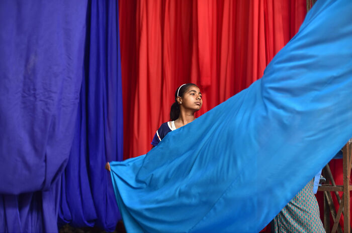 Young girl holding vibrant blue fabric against red and purple curtains in a candid moment of everyday life in Istanbul.
