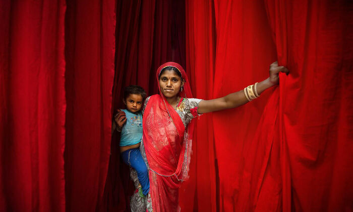 Woman in red fabric holding a child, captured in a candid moment of everyday life in Istanbul by Yücel Çetin.