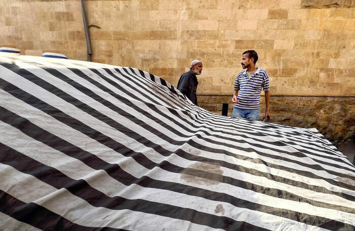 Two men talking behind a large black and white striped tarp, capturing candid moments of everyday life in Istanbul.