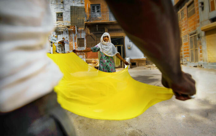 Two people stretching a bright yellow fabric in an outdoor urban setting, capturing candid moments of everyday life in Istanbul.