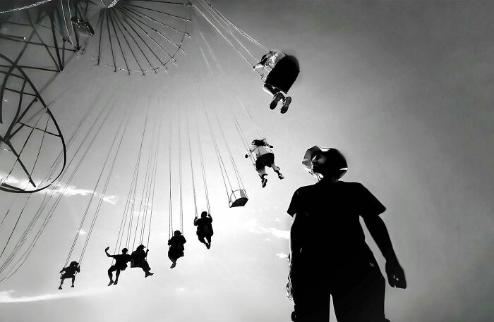 Black and white photo capturing candid moments of everyday life in Istanbul with people enjoying a swing ride against the sky.