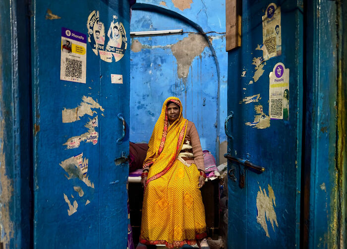 Woman in a yellow dress sitting in a weathered blue doorway, capturing candid moments of everyday life in Istanbul.