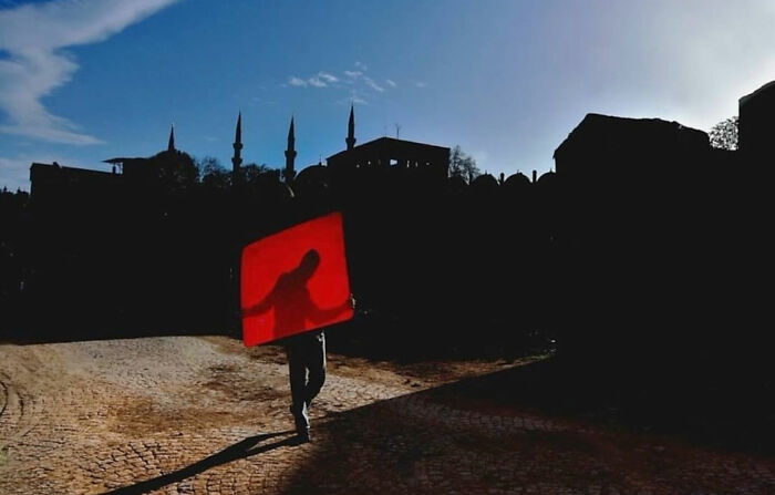 Silhouette of a person carrying a red sign on a cobblestone street in Istanbul during a candid moment.