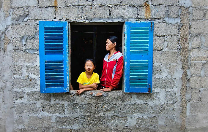 Two people seen through a blue window frame in a stone wall, capturing candid moments of everyday life in Istanbul.