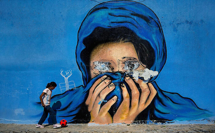Child playing with a red ball near a vibrant street mural depicting a veiled face in Istanbul everyday life scene.