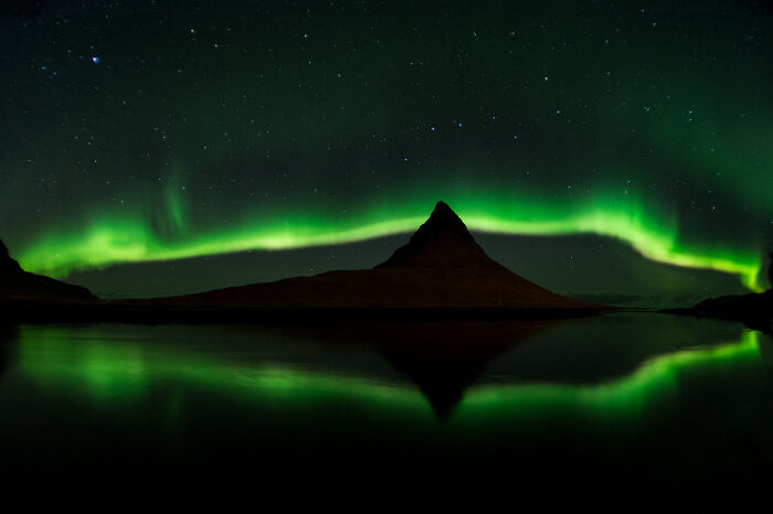 Northern lights glowing above a mountain reflected in calm water, showcasing stunning wildlife and nature scenery.